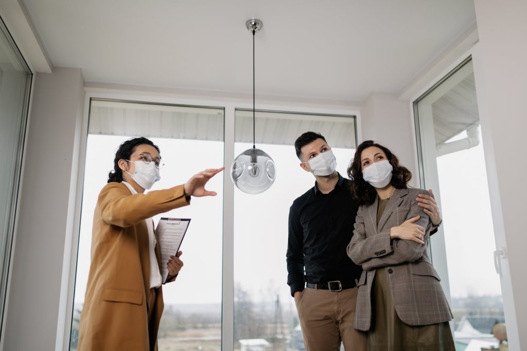 Estate agent showing masked couple a modern home interior during a property viewing amidst COVID-19 pandemic precautions