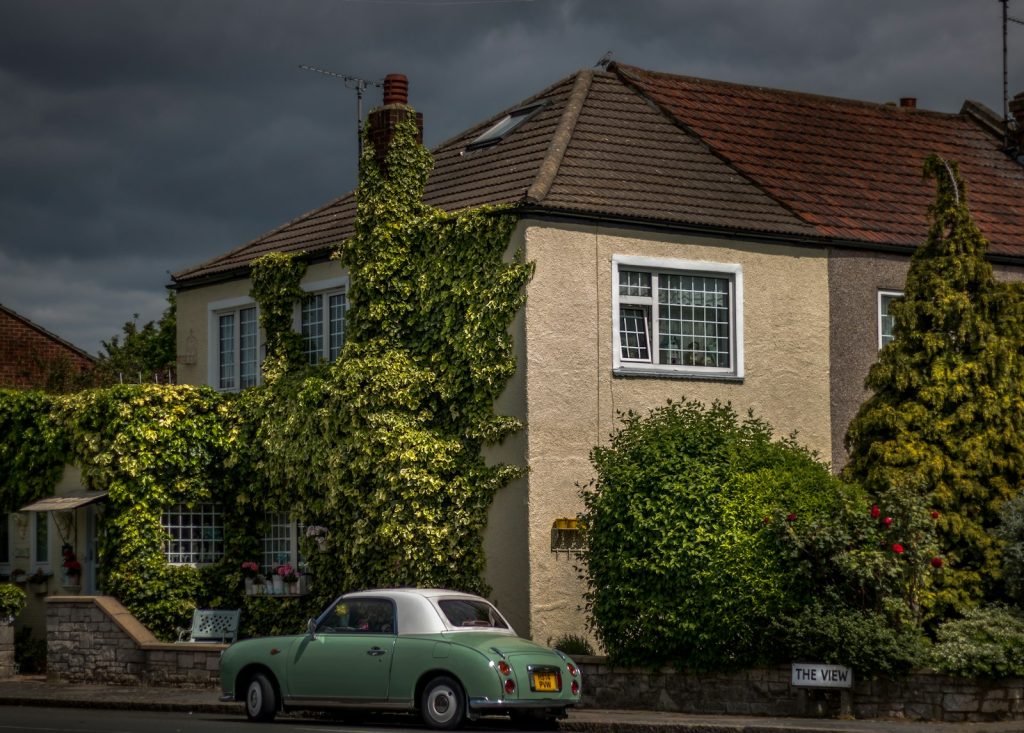 Vintage car parked outside ivy-covered house on a cloudy day, showcasing classic architecture in a serene neighbourhood