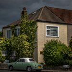 Vintage car parked outside ivy-covered house on a cloudy day, showcasing classic architecture in a serene neighbourhood