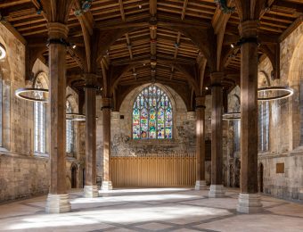 Historic cathedral hall interior with stained glass windows, wooden beams, and ring lights, showcasing medieval architecture