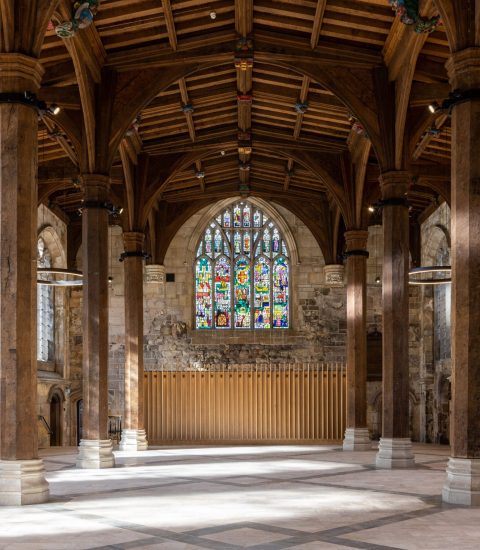 Historic cathedral hall interior with stained glass windows, wooden beams, and ring lights, showcasing medieval architecture