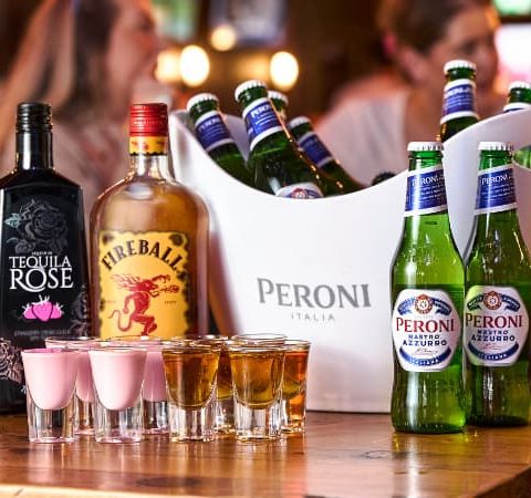 Variety of drinks on a pub table: Tequila Rose, Fireball whisky, Peroni beer bottles, and shots ready for a party atmosphere