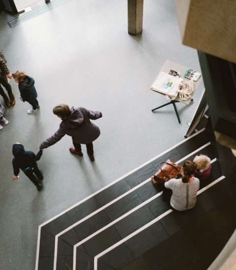 People interacting in an indoor space with children, viewed from above, near a table and stairs in a public building setting