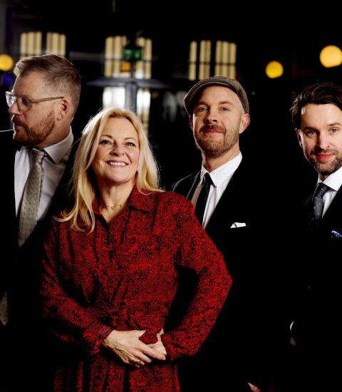 Group of four people in formal attire, smiling in an elegant setting, showcasing business or event professionals