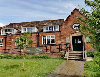 Historic brick building with manicured lawn and trees, displaying sign for Clements Hall, a community venue in York