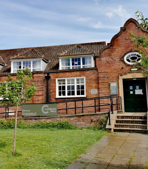 Historic brick building with manicured lawn and trees, displaying sign for Clements Hall, a community venue in York