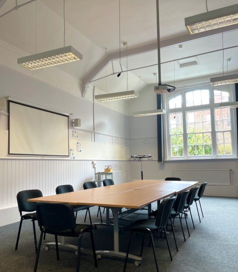 Spacious meeting room with wooden conference table, black chairs, projector, and large window letting in natural light