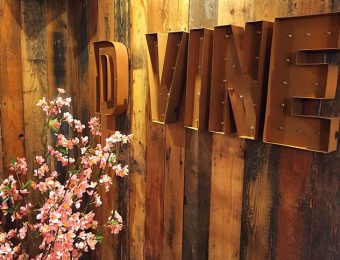 Rustic wooden wall with illuminated D VINE sign and pink cherry blossoms in the foreground for a cosy ambience