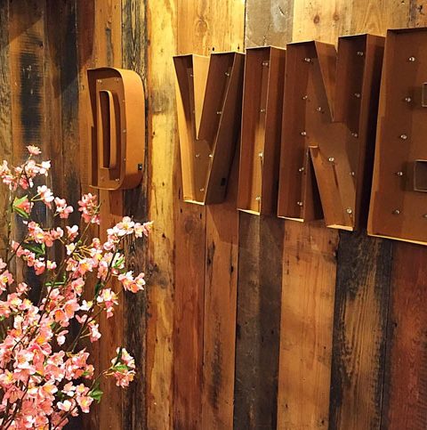 Rustic wooden wall with illuminated D VINE sign and pink cherry blossoms in the foreground for a cosy ambience