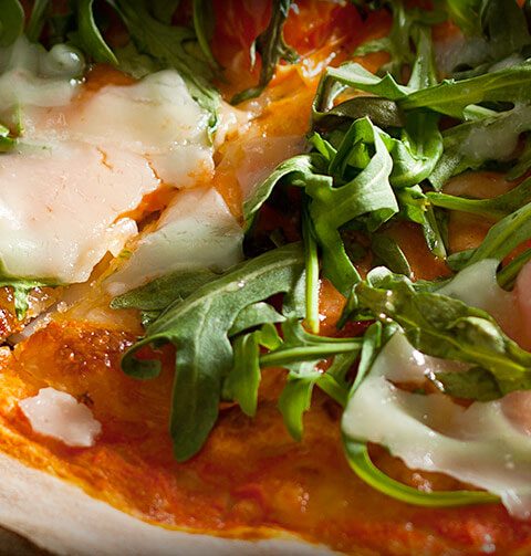 Close-up of a delicious pizza topped with fresh rocket and melted cheese on a wooden table, ideal for food enthusiasts