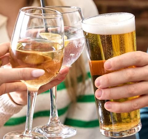 People toasting with various drinks, including beer and wine, while celebrating together in a casual setting