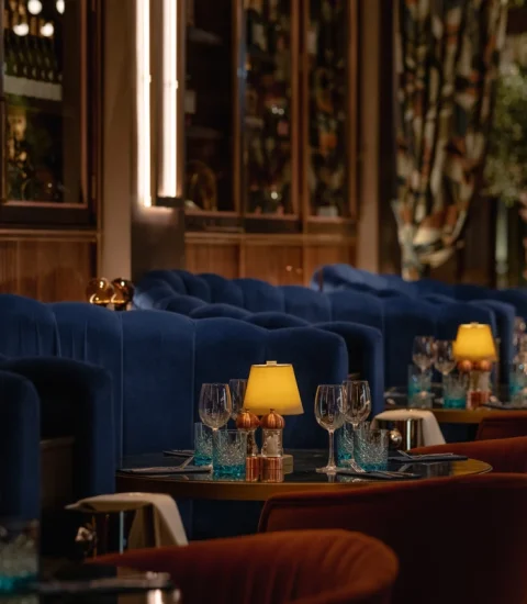 Elegant restaurant interior with blue velvet seating, soft lighting, and tables set with glasses and decorations