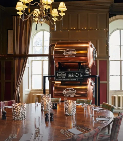 Vintage dining room with Pilsner Urquell tank beer, elegant chandelier, wooden table, and cosy ambiance
