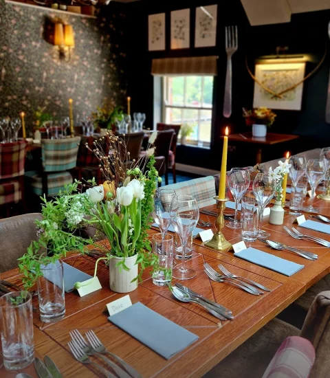 Elegant dining room with rustic decor, set for dinner with floral centrepieces, candles, and place settings on a wooden table