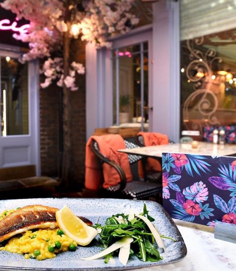 Plated seafood dish with lemon and greens at an elegant restaurant setting featuring floral decor and cosy seating