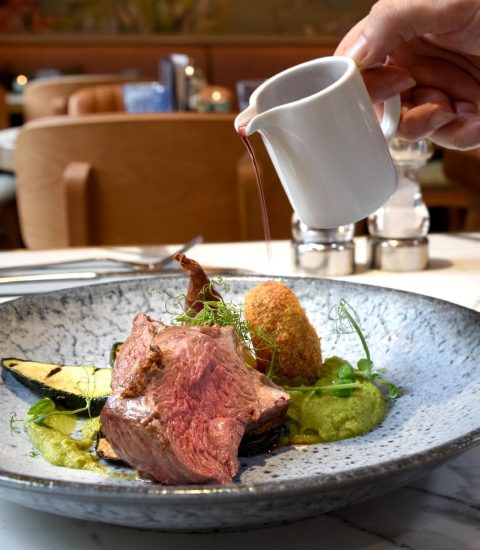 Elegant restaurant meal featuring succulent beef with sauce, plated with vegetables and a crispy potato croquette
