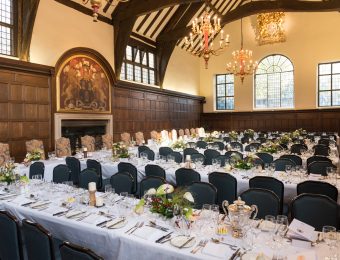Elegant banquet hall with long tables set for a formal event, featuring ornate chandeliers and historic wood panelling