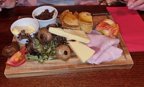 Ploughman's lunch with cheese, pork pies, ham, mushrooms, chutney, salad, and apple on a wooden board.