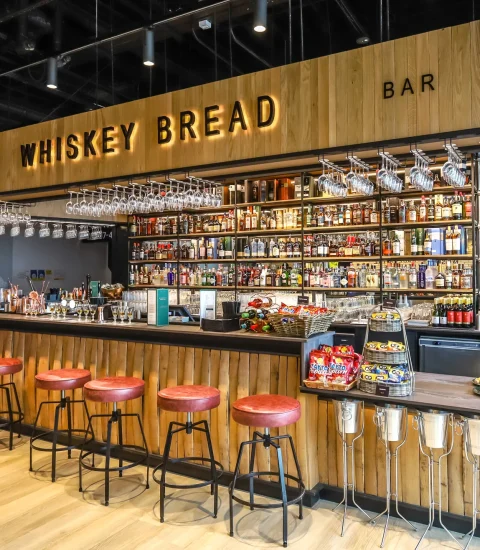 Trendy whiskey bar interior with wooden decor, red stools, and an extensive selection of spirits behind the counter