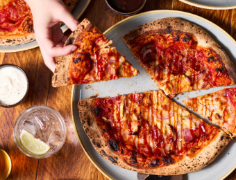 Hands sharing a deliciously cheesy pizza with drinks on a wooden table, ideal for a casual dining setting