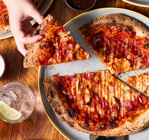 Hands sharing a deliciously cheesy pizza with drinks on a wooden table, ideal for a casual dining setting