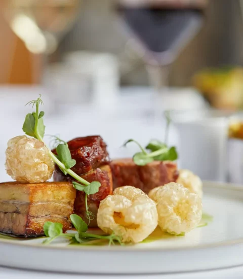 Gourmet dish with slow-cooked pork belly and crispy crackling, garnished with microgreens, served on a white plate