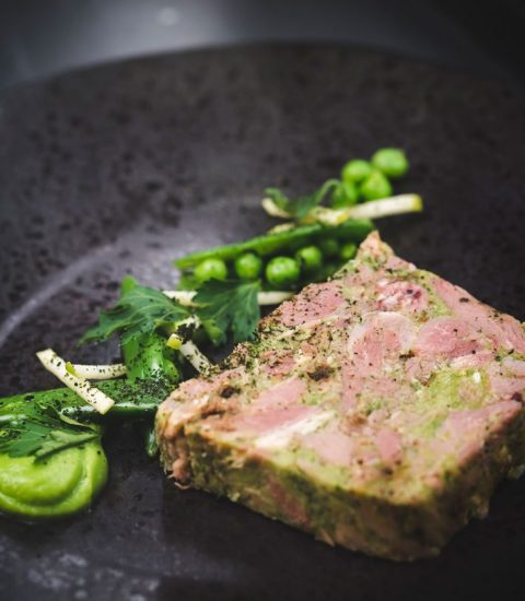 Gourmet meat terrine served with fresh greens on a dark plate, showcasing elegant fine dining presentation