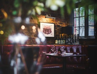 Cosy restaurant corner with leather seating, ambient lighting, and wine bottles on display in a rustic setting