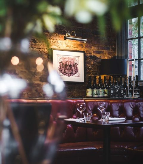 Cosy restaurant corner with leather seating, ambient lighting, and wine bottles on display in a rustic setting
