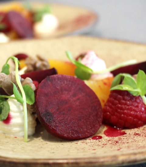 Gourmet beetroot salad with raspberries and cream, garnished with fresh microgreens on a rustic ceramic plate