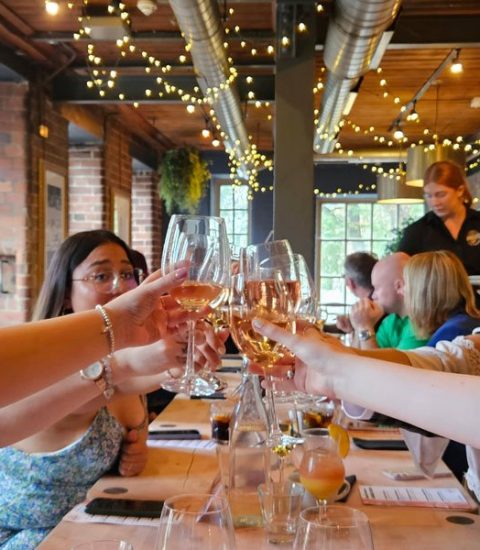 Friends celebrating with a toast in a cosy restaurant setting adorned with string lights and brick walls