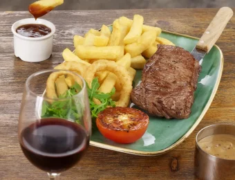 Steak, chips, onion rings, and grilled tomato on a plate with red wine and sauce, perfect for a classic meal out