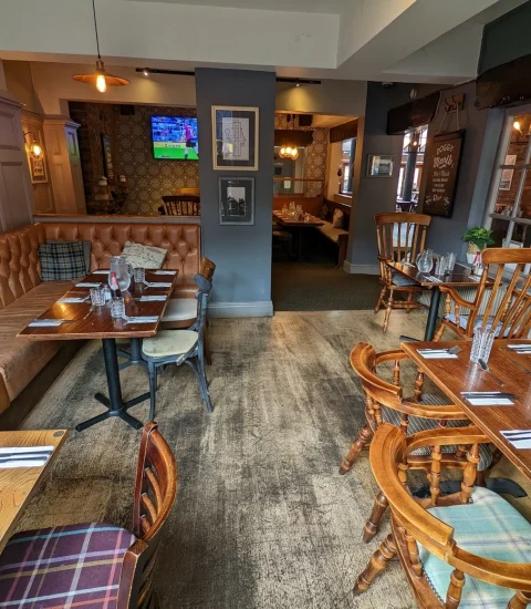 Cosy British pub interior with wooden tables, elegant seating, and sports on TV, set for dining with cutlery and glasses