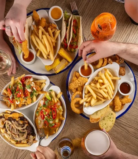 Overhead view of a table with friends enjoying fries, tacos, and assorted appetisers at a casual dining restaurant