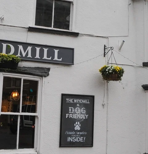 The Windmill pub exterior with hanging flowers, dog-friendly sign, promoting local cask ales in a charming UK setting