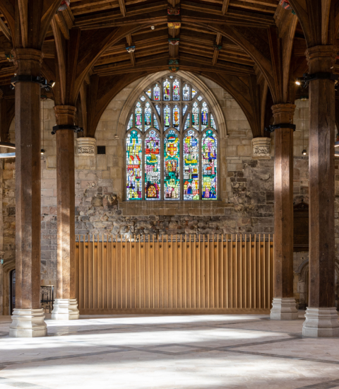 Historic cathedral interior with stained glass window, vaulted ceiling and stone pillars in sunlit medieval architecture