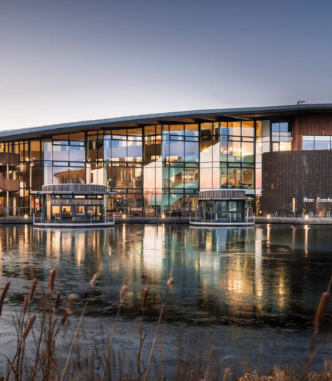 Modern architectural building with glass facade reflecting on a tranquil pond in evening light, showcasing urban design