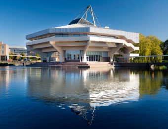Modern building reflected in a serene lake, set against a clear blue sky, showcasing innovative architecture at its finest