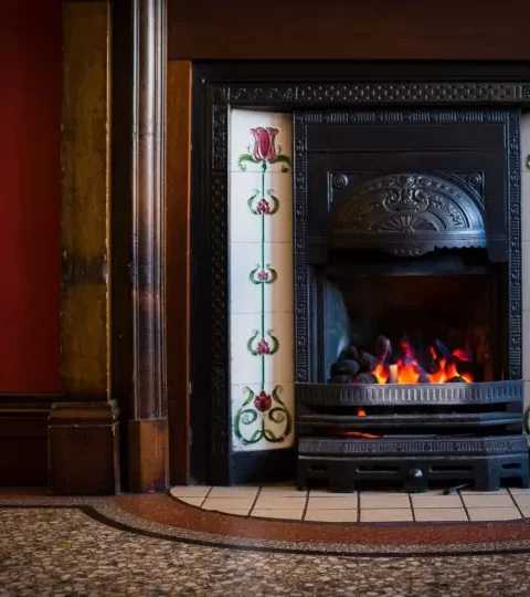 Victorian-style fireplace with ornate tiles and burning fire, creating a cosy and elegant atmosphere in a classic room