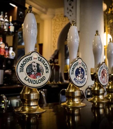Traditional pub beer taps featuring Timothy Taylor's ales on a wooden bar in a classic British pub setting