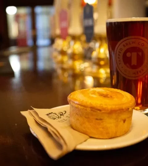 Pint of beer with tasty pie on bar counter in cosy UK pub setting