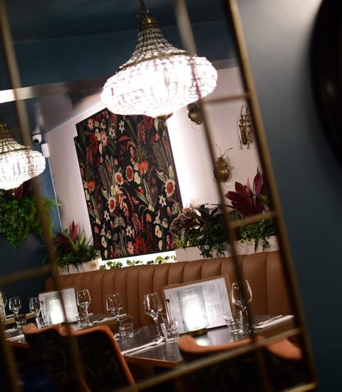 Chic restaurant interior with elegant lighting, floral decor, and set dining table reflected in mirror with vintage clock