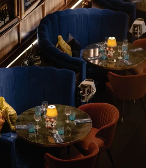 Elegant restaurant setting with plush blue booths, round tables, ambient lighting, and glassware, creating cosy dining atmosphere
