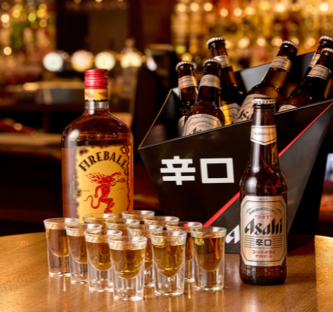 Selection of drinks on a bar: Fireball whisky, Asahi beer bottles, and shot glasses arranged on a wooden table