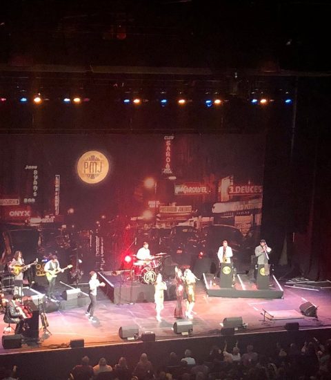 Live band performing on stage with vibrant cityscape backdrop, featuring musicians and illuminated atmospheric lighting