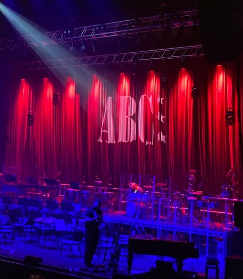 Concert stage setup with red lighting, instruments ready for ABC performance, creating a vibrant live music atmosphere