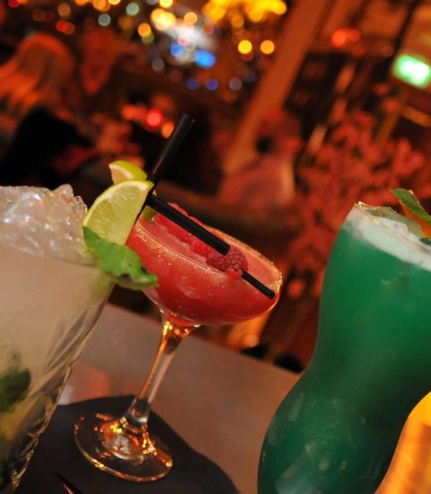Colourful cocktails with lime and mint garnish at a lively bar, perfect for a night out with friends or celebration