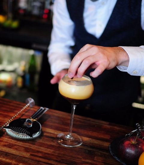 Bartender crafting a creamy cocktail at a bar, surrounded by shakers, strainer, and fresh fruit for garnish