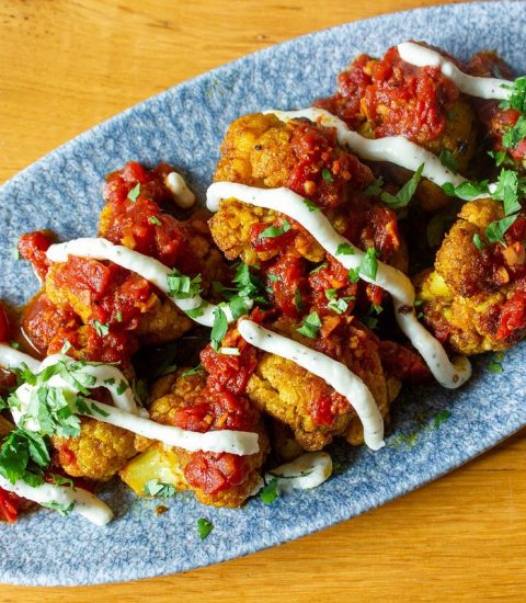 Spicy cauliflower bites with tomato sauce, drizzled with yoghurt and garnished with coriander on a blue plate