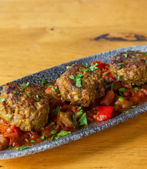 Three delicious meatballs garnished with herbs served on a platter with diced vegetables, showcasing Mediterranean cuisine